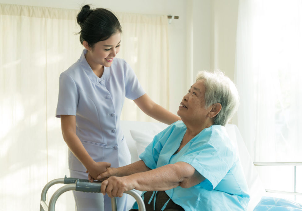 Asian young nurse supporting elderly patient disabled woman in using walker in hospital. Elderly patient care concept.