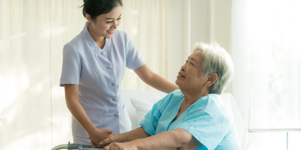 Asian young nurse supporting elderly patient disabled woman in using walker in hospital. Elderly patient care concept.