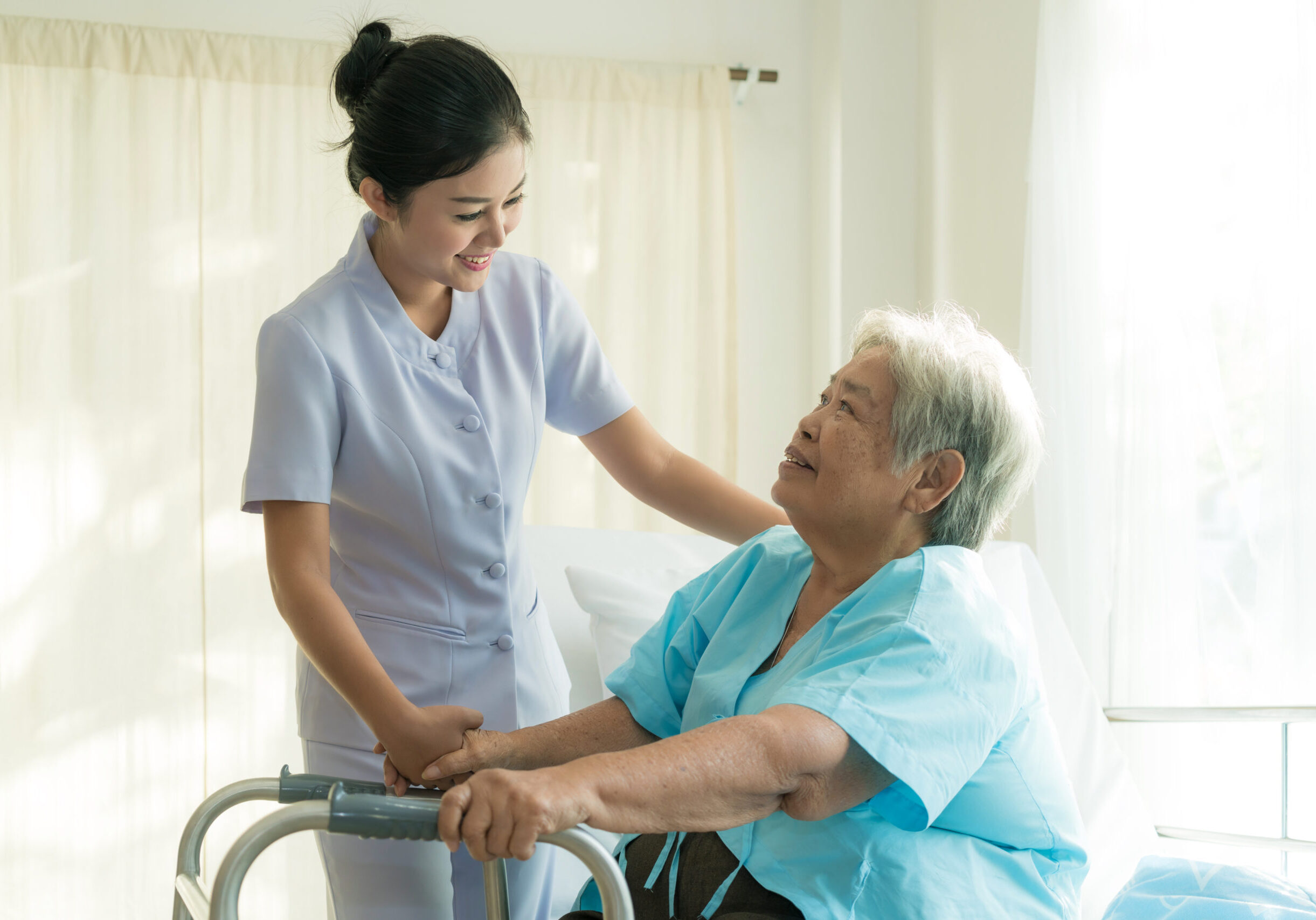 Asian young nurse supporting elderly patient disabled woman in using walker in hospital. Elderly patient care concept.