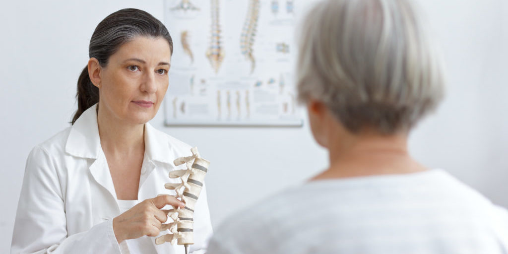 Aging and back pain concept: doctor of orthopedics showing her senior patient a slipped disk on a backbone model.