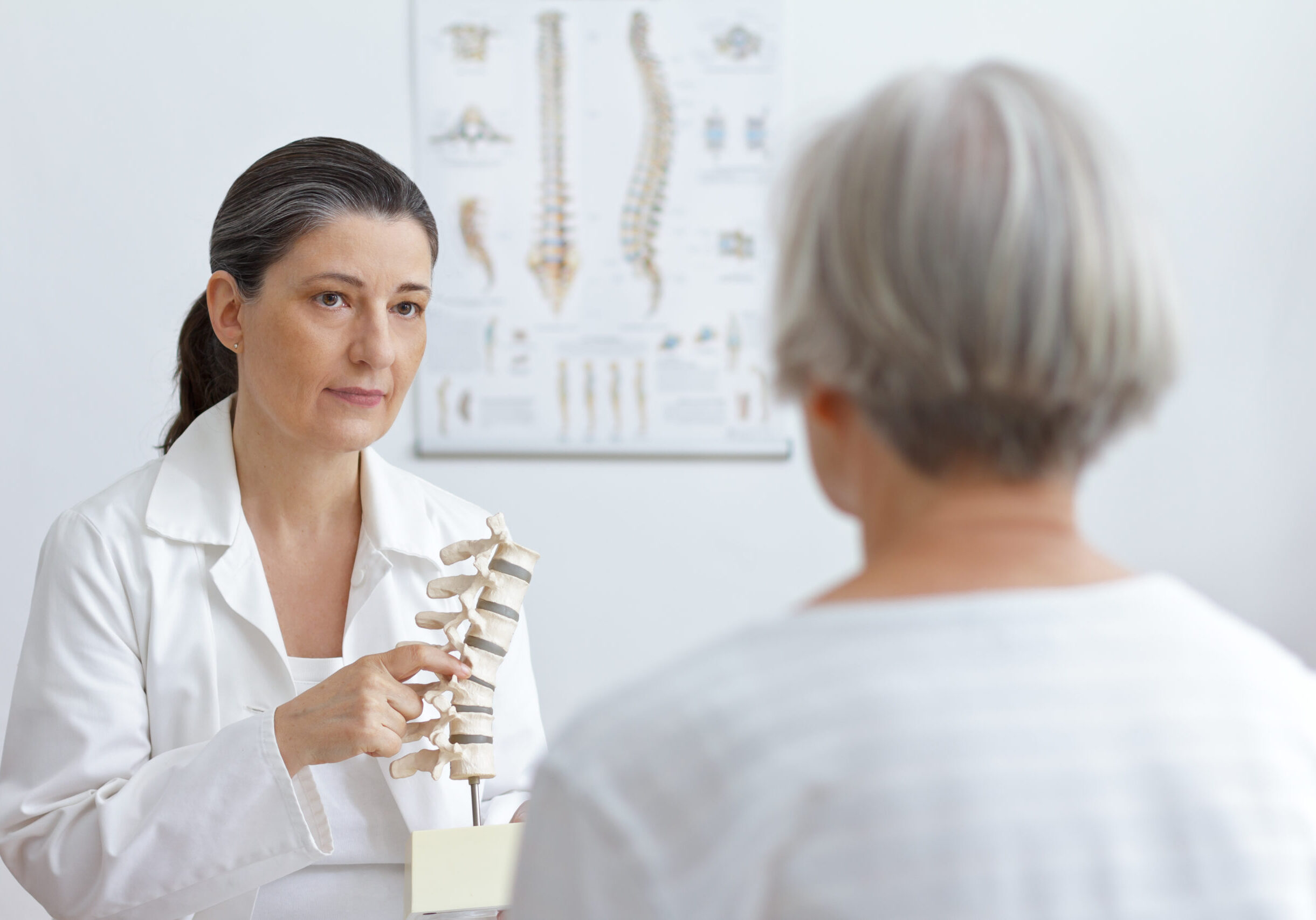 Aging and back pain concept: doctor of orthopedics showing her senior patient a slipped disk on a backbone model.